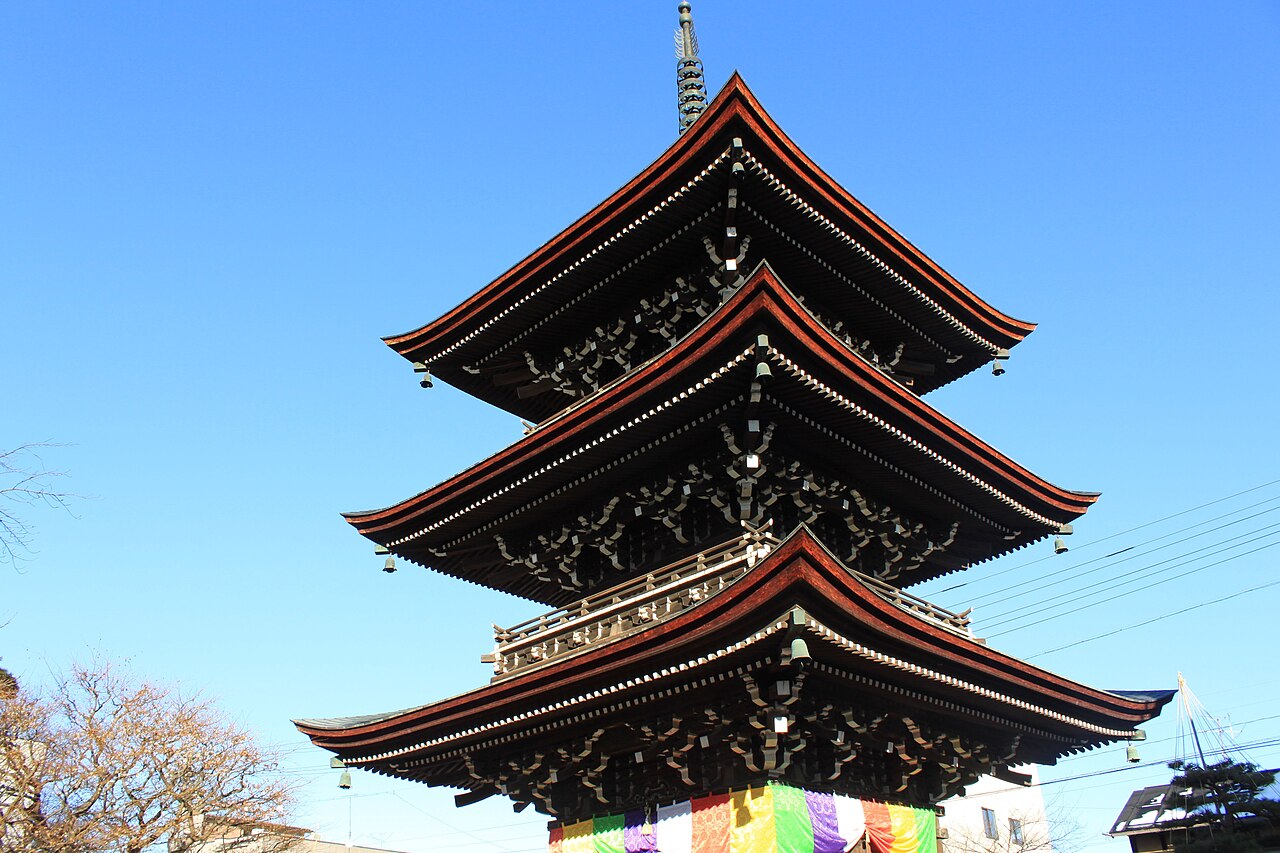 The three-storied wooden pagoda of Hida Kokubunji temple in Takayama, dark tiered roofs against a clear blue sky.