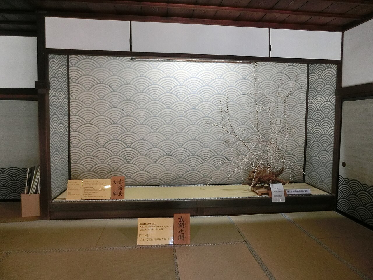 The genkan entrance room of Takayama Jinya with a blue-wave patterned screen behind a raised tatami platform and a small display of flowers.