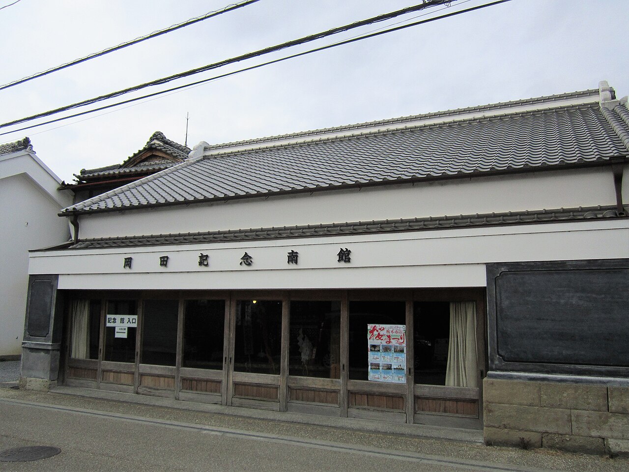 The tiled-roof front of the Okada Memorial South Hall in Tochigi, with wooden sliding glass doors and the hall name written in large characters above
