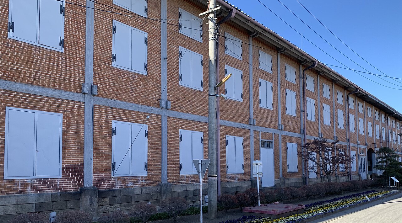 The long brick wall of the East Cocoon Warehouse at Tomioka Silk Mill, seen from the street with its rows of white shuttered windows