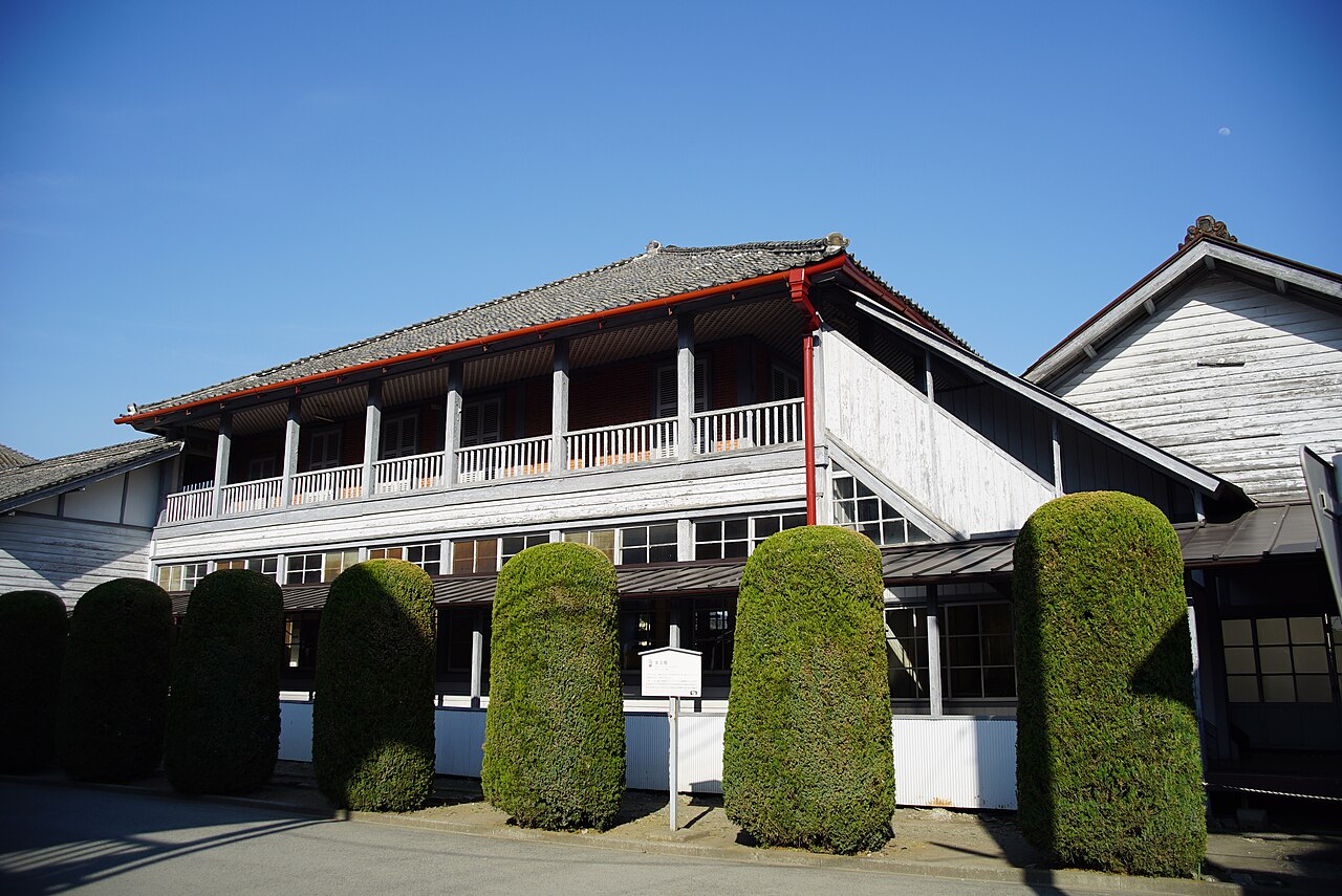 The Women's Instructors' House at Tomioka Silk Mill, a wooden building with a white upper gallery, behind clipped hedges under a blue sky