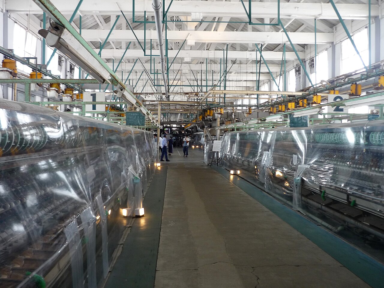 Inside the Reeling Hall at Tomioka Silk Mill, with rows of covered reeling machines along a central aisle and a few visitors at the far end