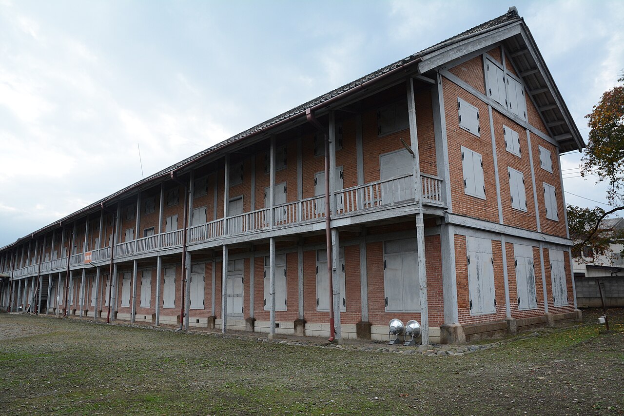 The West Cocoon Warehouse at Tomioka Silk Mill, a brick building with a wooden upper gallery, seen across the lawn