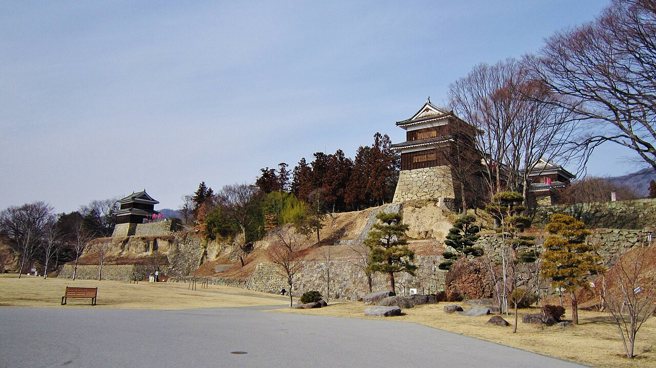 Two turrets of Ueda Castle on a stone-walled earthen bank above a bare winter lawn