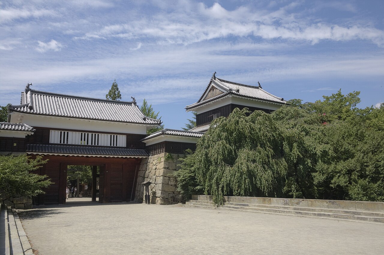The tiled Higashi-koguchi gatehouse of Ueda Castle with a corner turret and a stone-faced base, under a blue summer sky