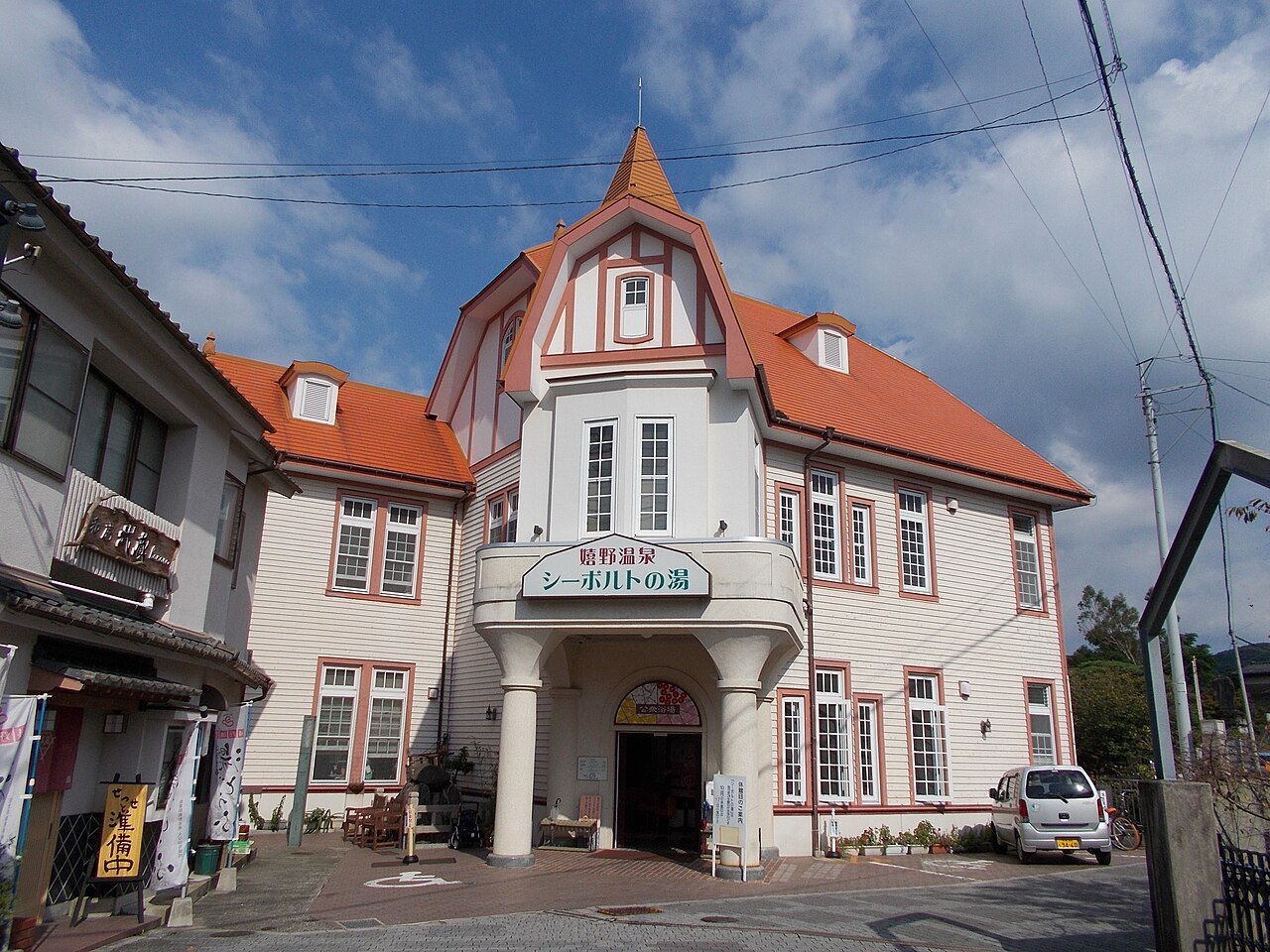 Siebold no Yu public bath in Ureshino Onsen, a white timber building with an orange roof and a pointed tower under a blue sky