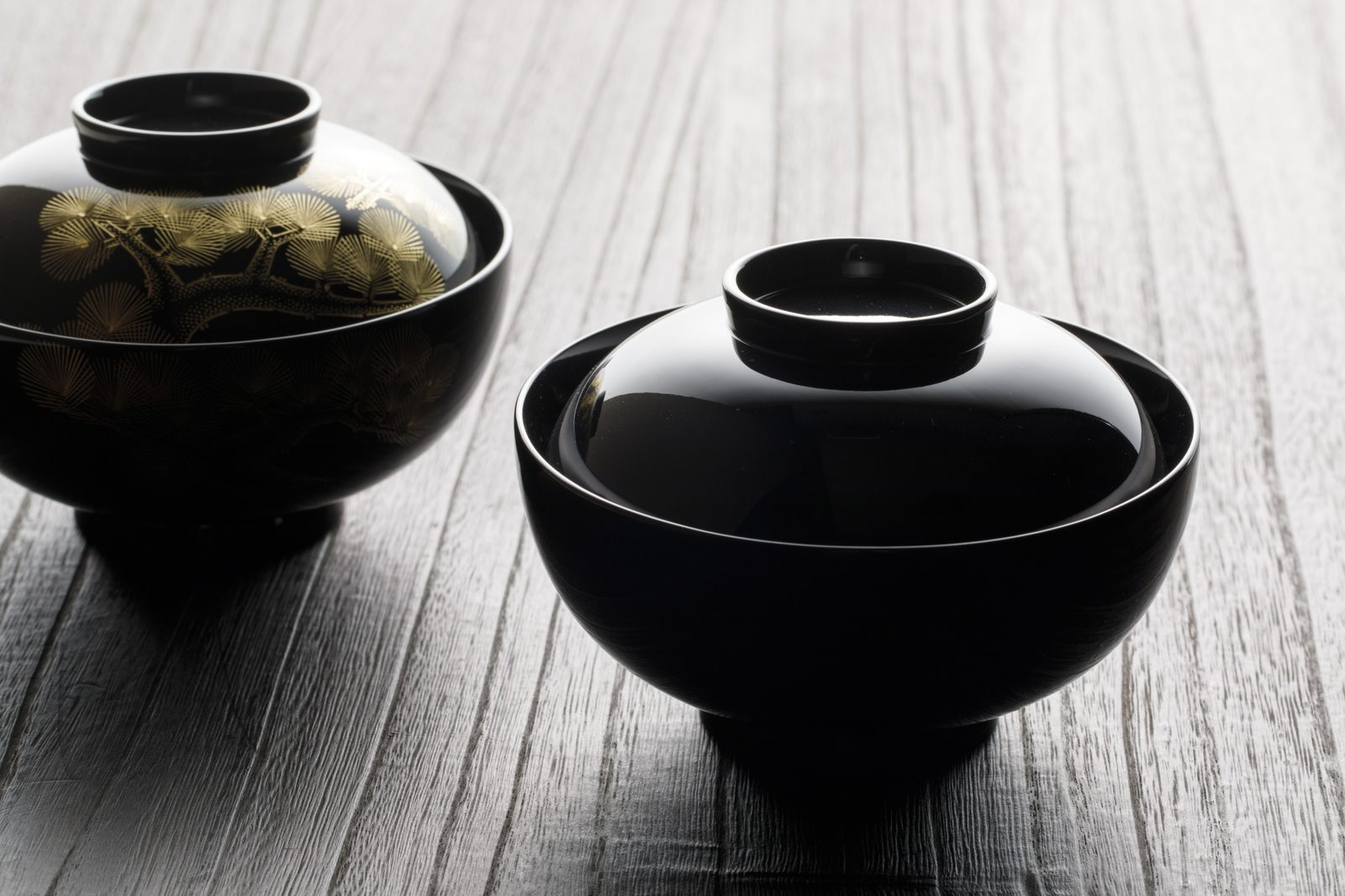 Two black Wajima-nuri lacquer soup bowls with lids, one decorated with gold maki-e