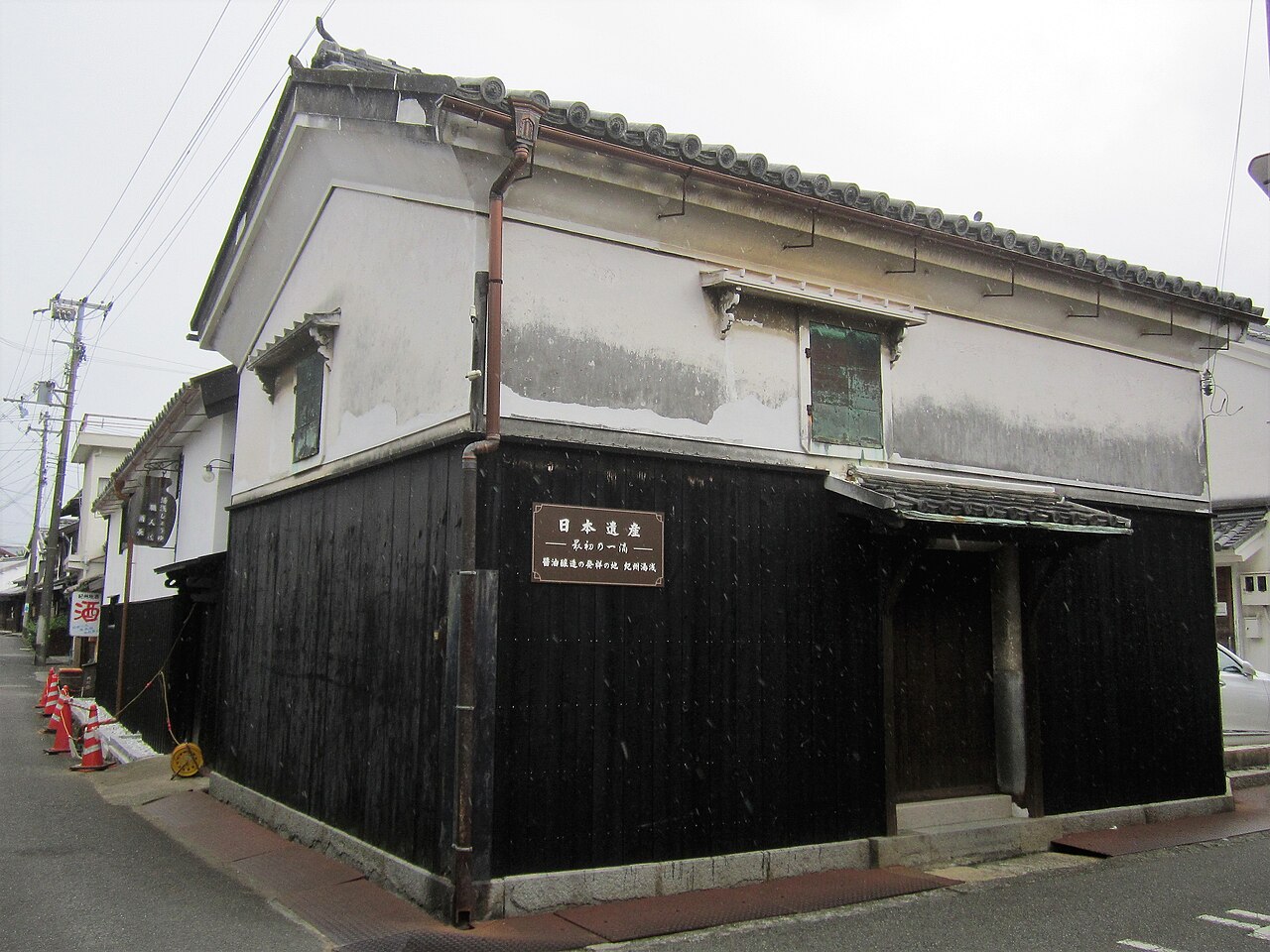 Black-plank wall and white plaster upper storey of an old storehouse beside a quiet street in Yuasa