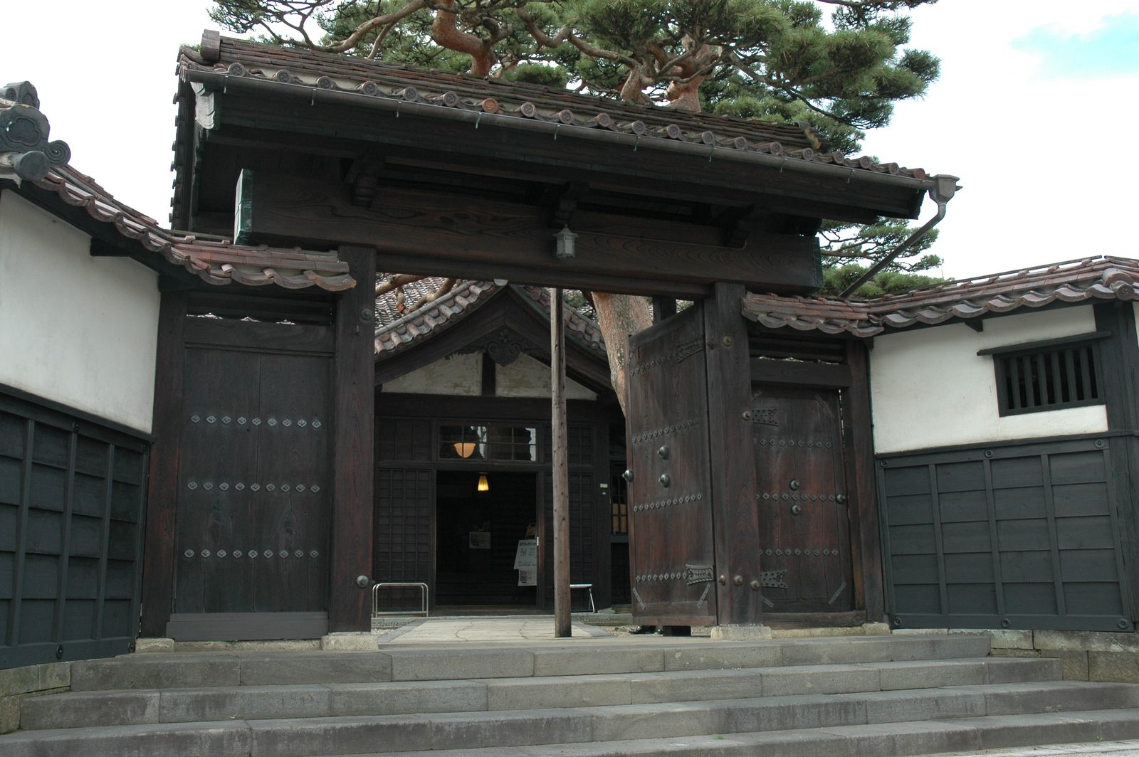 Wooden gate of the former Homma family residence set in a wall of white plaster and black boards