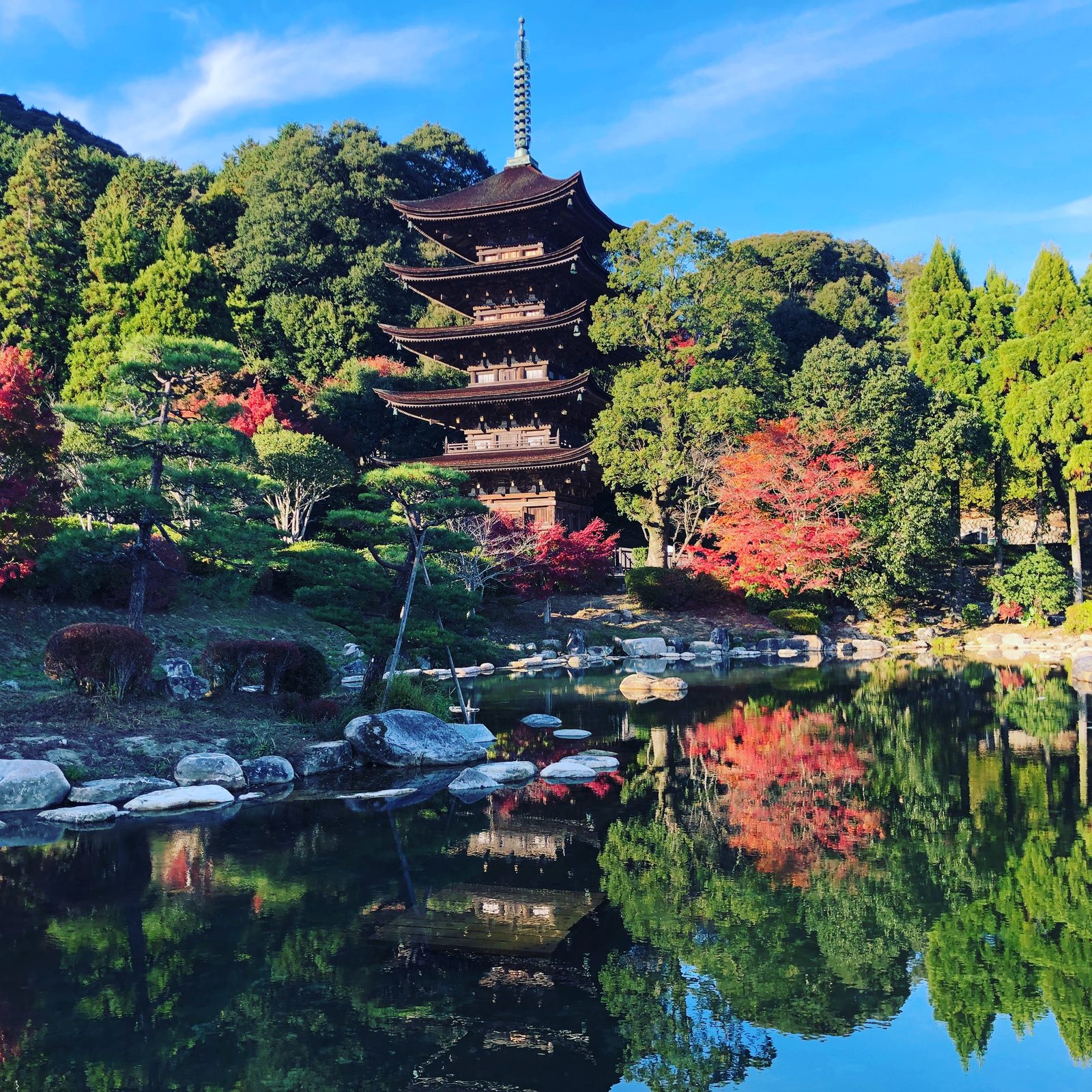 The five-storied wooden pagoda of Rurikoji rising above a garden pond, with red maples and green trees reflected in the water