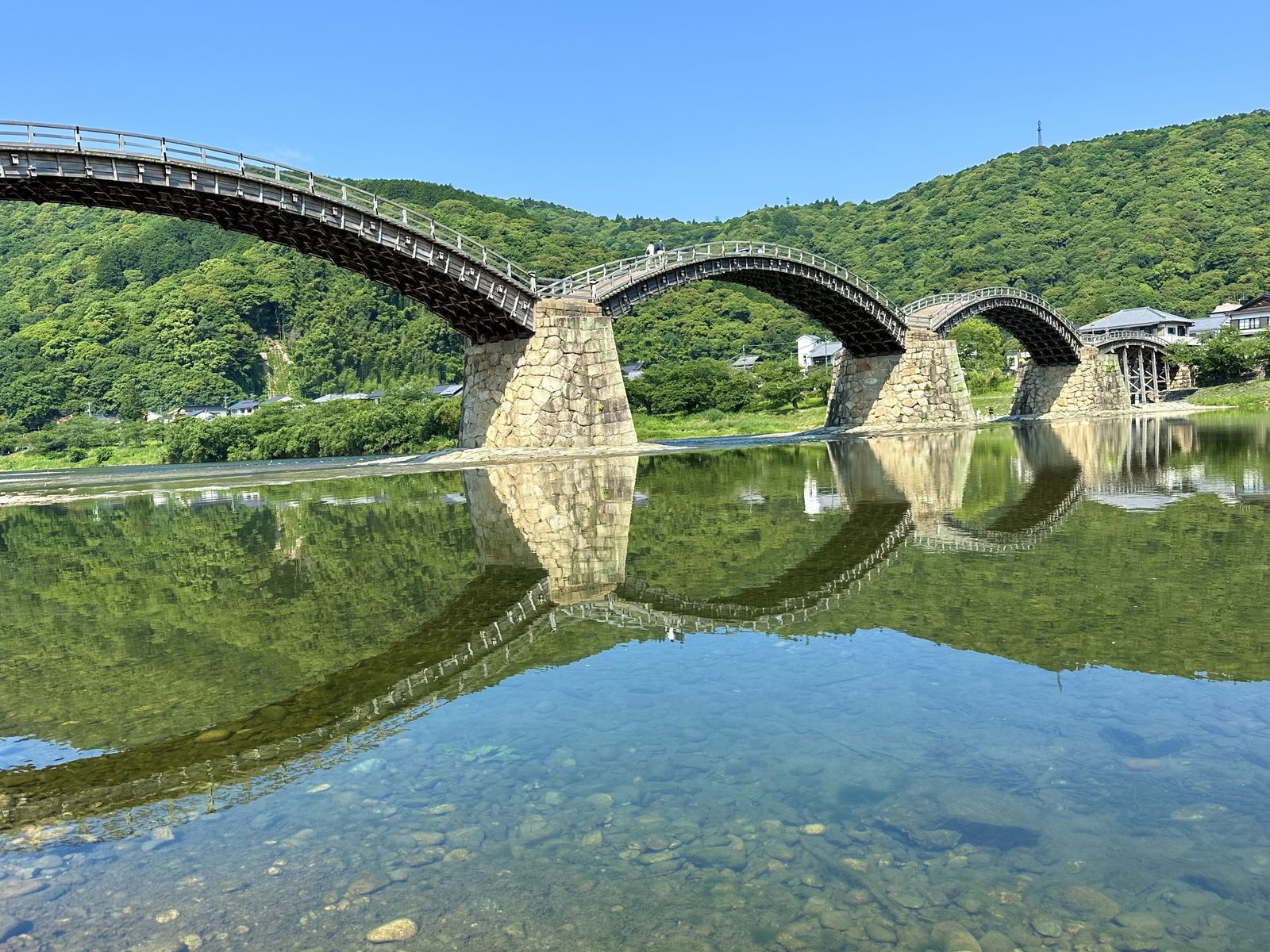 The five arches of Kintaikyo Bridge reflected in the clear Nishiki River on a sunny day