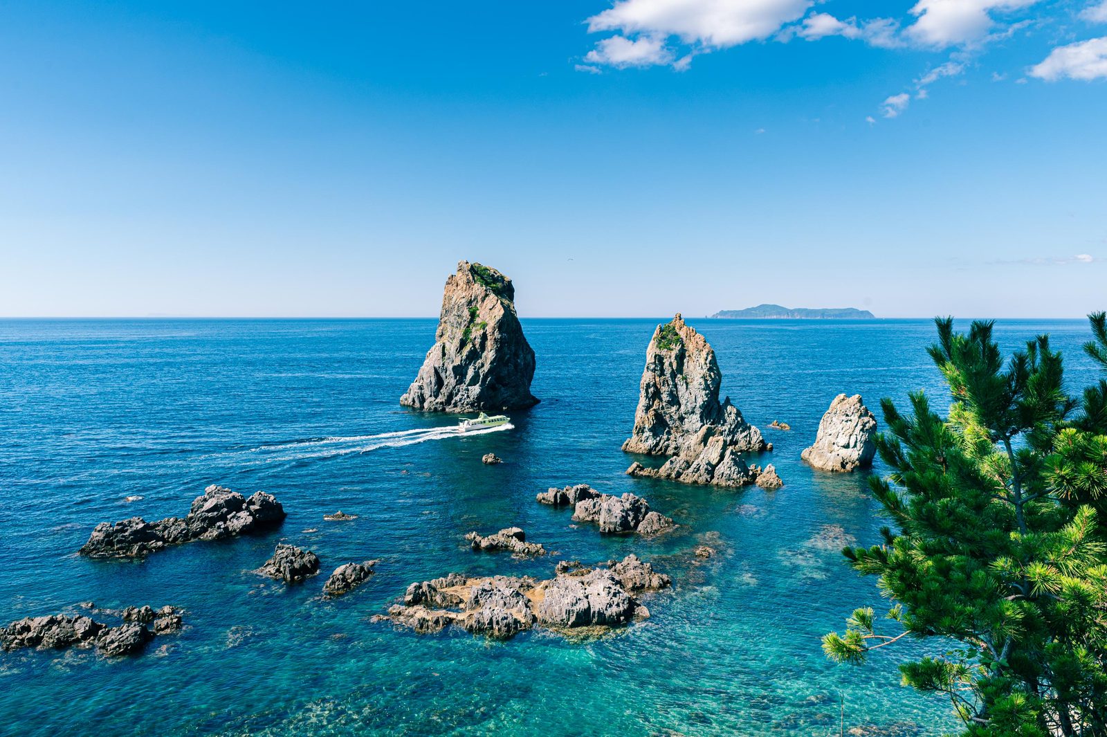 Sea stacks seen from a sightseeing boat off Omijima island in Nagato, with a boat wake across the blue sea