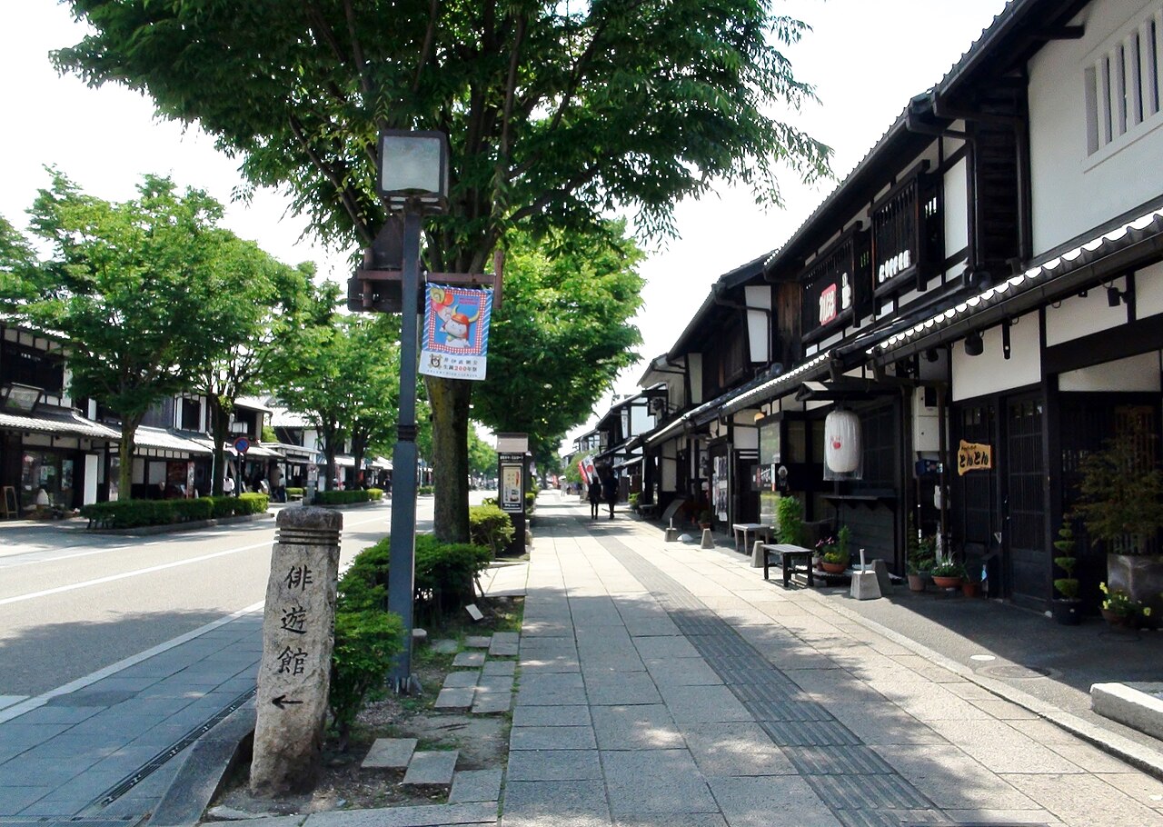 The black-and-white timbered shopfronts of Yume Kyobashi Castle Road in Hikone, a quiet paved street lined with trees near the castle.